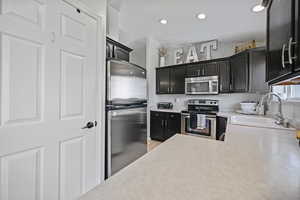 Kitchen with light countertops, a sink, dark cabinetry, stainless steel appliances, and recessed lighting