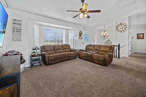 Living room featuring visible vents, baseboards, lofted ceiling, ceiling fan with notable chandelier, and carpet floors