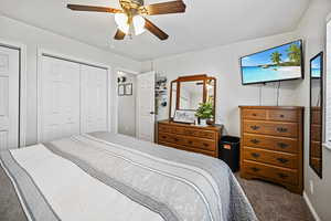 Bedroom with multiple closets, a ceiling fan, and carpet