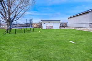 View of yard with a trampoline, an outbuilding, and fence