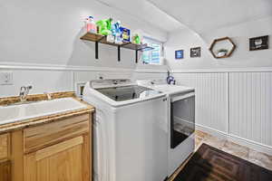 Laundry room with washing machine and dryer, a textured ceiling, a sink, and wainscoting