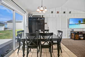 Dining area featuring light tile patterned floors, vaulted ceiling, a notable chandelier, and light carpet