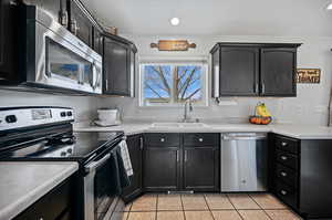 Kitchen with light countertops, appliances with stainless steel finishes, a sink, dark cabinets, and light tile patterned floors