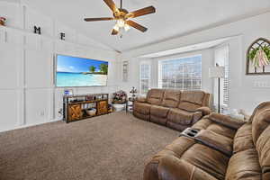 Living room with carpet flooring, a decorative wall, vaulted ceiling, and ceiling fan