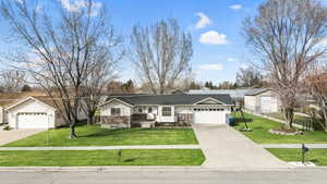Single story home with an attached garage, a shingled roof, a front lawn, and concrete driveway