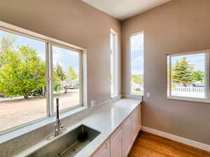 Kitchen featuring baseboards, light stone counters, light wood-style flooring, white cabinets, and a sink