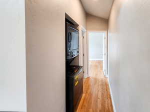Hallway with baseboards, stacked washer / drying machine, light wood-style floors, and a textured wall