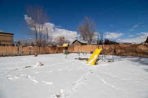 Snow covered playground featuring a playground and a fenced backyard