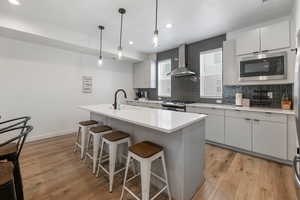 Kitchen with light wood-style flooring, stainless steel appliances, a kitchen breakfast bar, wall chimney exhaust hood, and tasteful backsplash