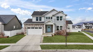 View of front of house featuring board and batten siding, a front lawn, fence, concrete driveway, and stone siding