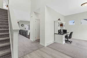 Office with visible vents, baseboards, a towering ceiling, and light carpet