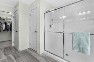 Full bathroom with baseboards, a spacious closet, wood finished floors, and a shower stall