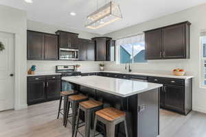 Kitchen with light wood-type flooring, a kitchen bar, light countertops, stainless steel appliances, and a sink