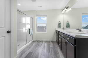 Full bathroom featuring double vanity, visible vents, wood finished floors, and a sink