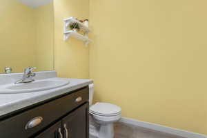 Bathroom featuring baseboards, toilet, wood finished floors, and vanity