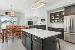 Kitchen featuring light wood finished floors, a kitchen island, glass insert cabinets, light countertops, and freestanding refrigerator