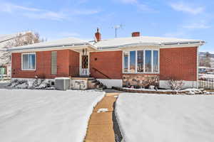 View of front of house with central AC unit, brick siding, and a chimney