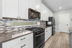 Kitchen featuring backsplash, white cabinetry, black appliances, and light wood-type flooring
