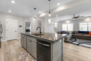 Kitchen with dark countertops, light wood-style flooring, appliances with stainless steel finishes, a upgraded ceiling fan, and a sink