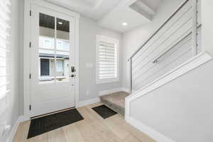 Inside front door, entryway featuring, canister lighting, windows, large plantation shutters, light wood-type flooring, large baseboards, and modern design metal railing, stairs to main floor