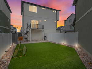 Back of property at dusk with spiral stairway and balcony, a yard, vinyl fencing, turf field