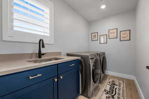 Clothes washing area featuring window, large plantation shutters, large baseboards, wood type floor, granite counter top sink, canister lights