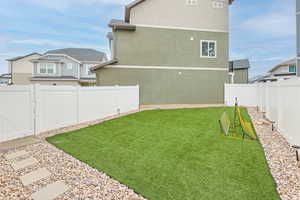 View of backyard, vinyl fence, turf field, a gate, gravel and pavers