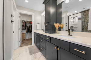 Master Bathroom featuring side by side vanity sinks, granite counter tops, walk in closet with organizer, marble finish floor, and a shower stall