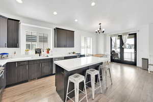 Kitchen featuring a sink, stainless steel dishwasher, a kitchen breakfast bar, a notable chandelier, and light wood-type flooring