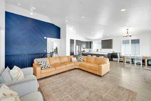 Living area featuring vaulted ceiling, light wood-style flooring, a notable chandelier, and recessed lighting