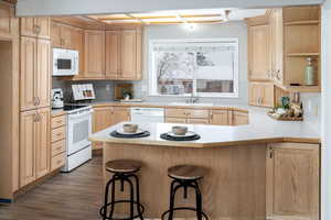 Kitchen with white appliances, light brown cabinets, a peninsula, open shelves, and a sink