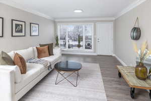 Living room with wood finished floors, baseboards, and ornamental molding