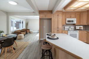 Kitchen with white appliances, a breakfast bar area, wood finished floors, baseboards, and light countertops