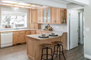 Kitchen featuring dishwasher, a breakfast bar area, light countertops, light wood-style flooring, and a sink