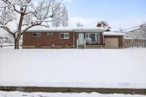 Snow covered back of property with brick siding, a chimney, a garage, and fence