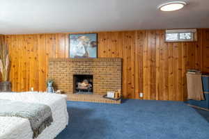 Bedroom featuring a brick fireplace, wooden walls, and carpet