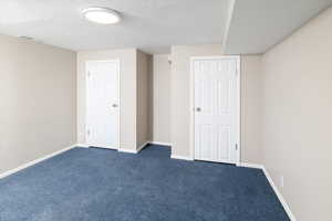 Interior space featuring baseboards, visible vents, dark carpet, and a textured ceiling