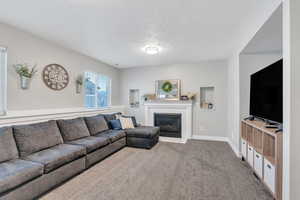Living room featuring baseboards, carpet, a fireplace, and a textured ceiling