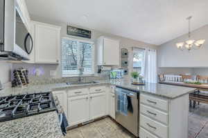 Kitchen with appliances with stainless steel finishes, a peninsula, an inviting chandelier, white cabinets, and a sink