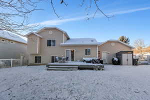 Snow covered house featuring an outbuilding, a deck, a storage shed, and fence