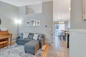 Living room featuring light tile patterned floors, baseboards, visible vents, high vaulted ceiling, and a notable chandelier
