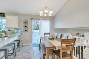 Dining area with vaulted ceiling, light tile patterned floors, baseboards, and a chandelier