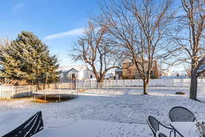 Snowy yard featuring a residential view, a trampoline, and a fenced backyard