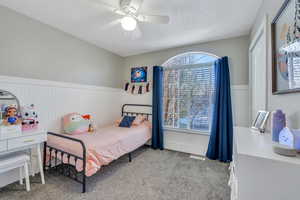 Bedroom featuring ceiling fan, a textured ceiling, carpet flooring, and wainscoting