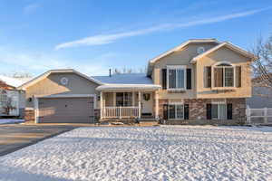 Tri-level home featuring a garage, brick siding, driveway, and stucco siding
