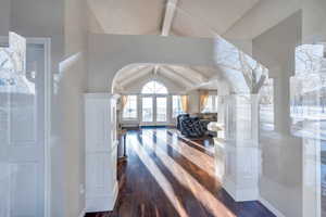 Hallway with beam ceiling, dark wood-style floors, french doors, arched walkways, and high vaulted ceiling