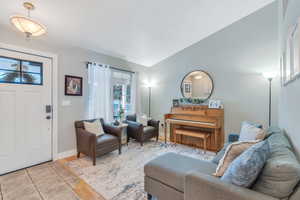 Living area with baseboards, light tile patterned flooring, and vaulted ceiling