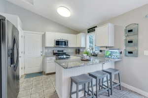 Kitchen featuring light tile patterned floors, light stone countertops, a peninsula, stainless steel appliances, and white cabinetry