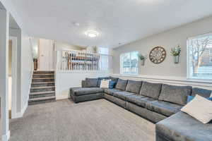Carpeted living room with stairway, a textured ceiling, and baseboards