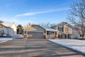 Split level home featuring stucco siding, driveway, a porch, fence, and an attached garage